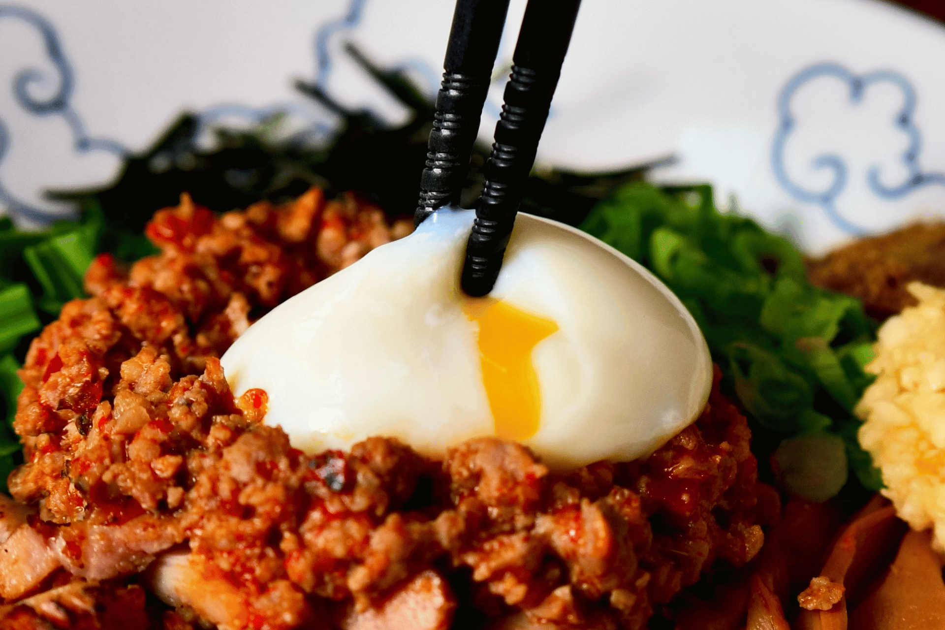 The poached egg being mixed through RAMEN RAIJIN Spicy Taiwanese Mazesoba, turning the spicy minced pork mellow and glossy