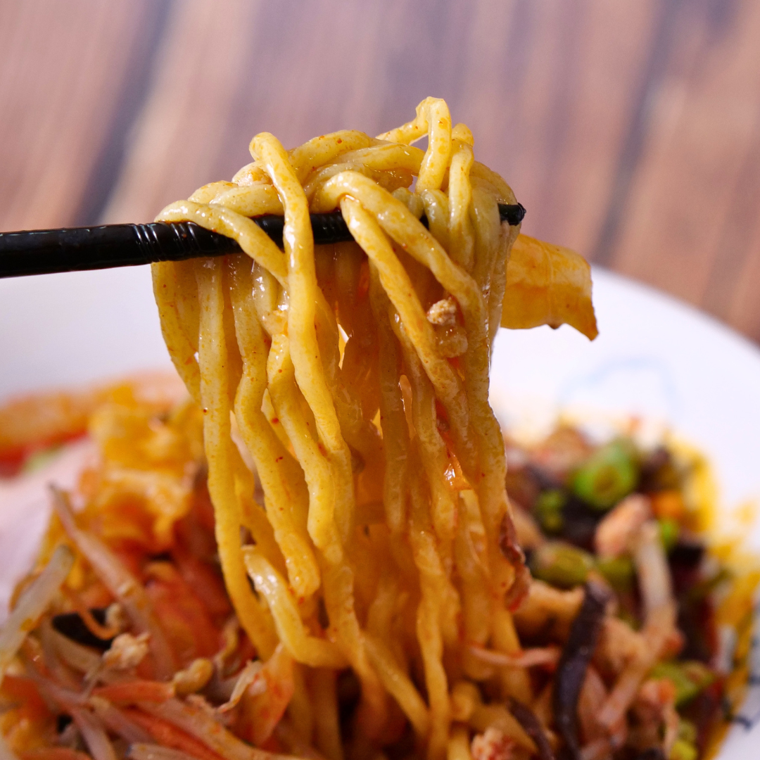 Fresh ramen noodles lifted from a bowl of RAMEN RAIJIN Frozen Spicy Shio Tanmen